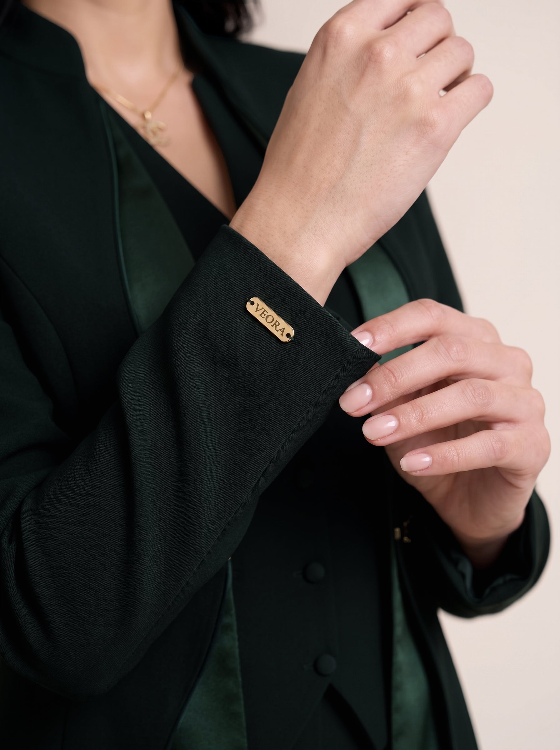TERRA sleeve cuff close-up with the gold-tone VEORA nameplate and crepe fabric texture.